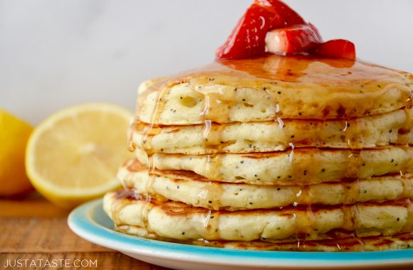 Lemon Poppyseed Pancakes topped with strawberries and maple syrup on blue plate with half a lemon in background.