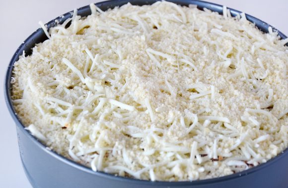 Springform pan with rigatoni pie topped with shredded mozzarella and Parmesan