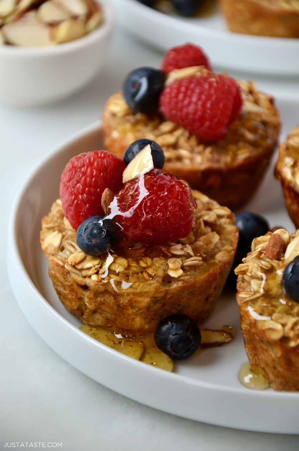 Baked oatmeal muffins drizzled with warm maple syrup and topped with fresh berries and sliced almonds.