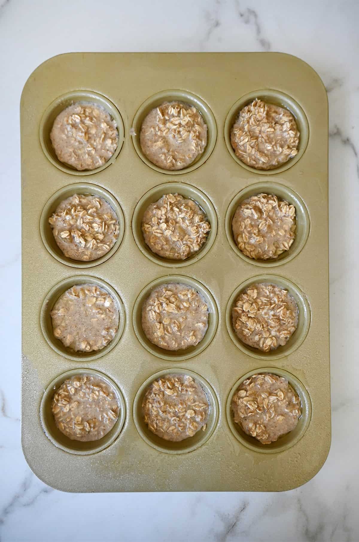 A muffin pan filled with an oatmeal mixture featuring mashed bananas, milk and cinnamon.