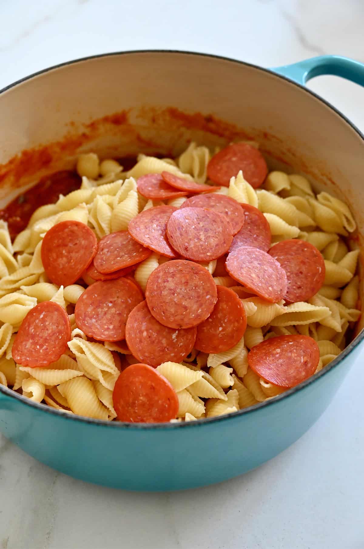 Combining cooked pasta, marinara sauce, cooked sausage, diced peppers and onions, and pepperoni in a Dutch oven.