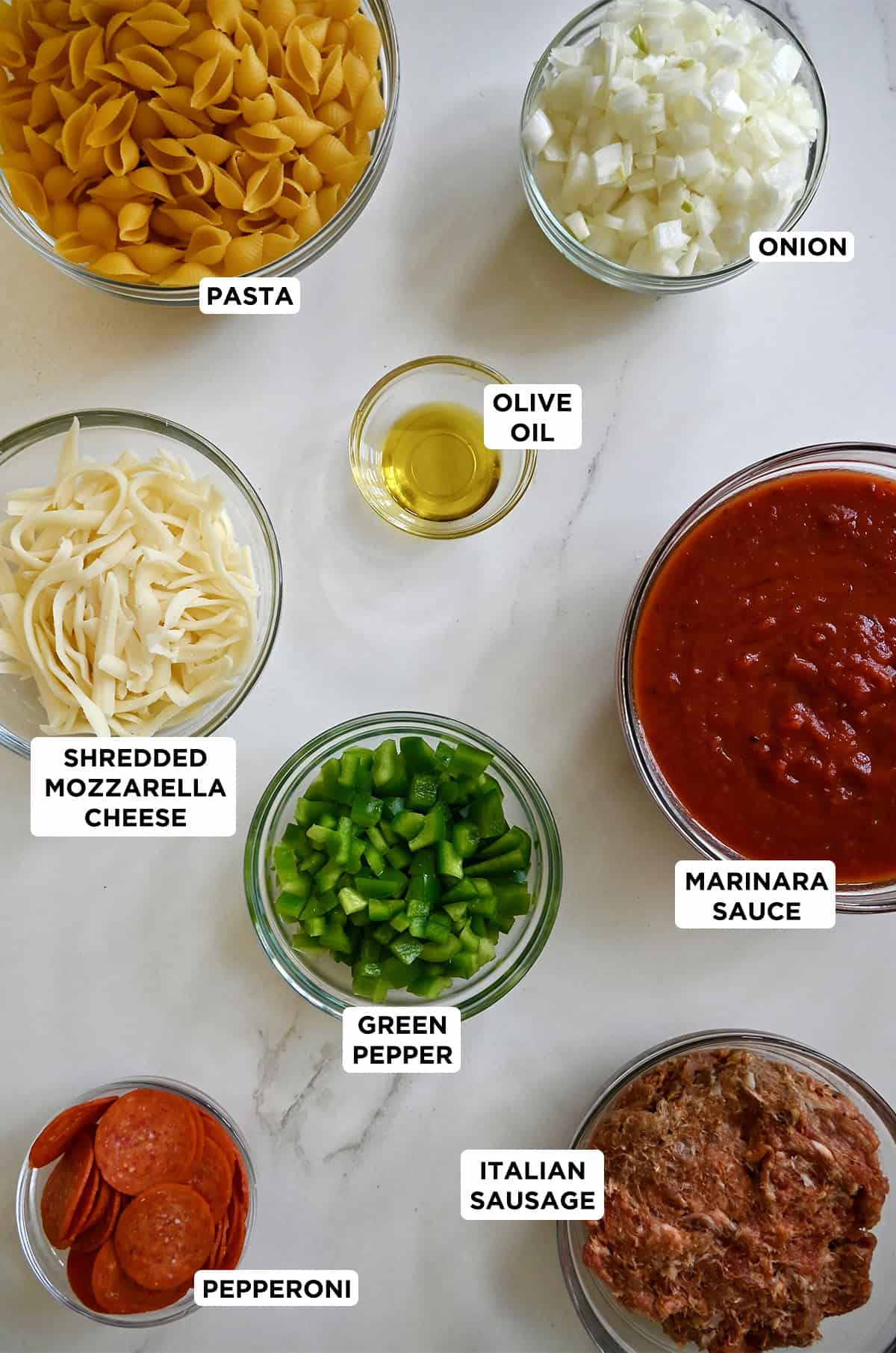 Ingredients to make pizza casserole, including short pasta, marinara sauce, diced green peppers, mini pepperoni and shredded mozzarella cheese.
