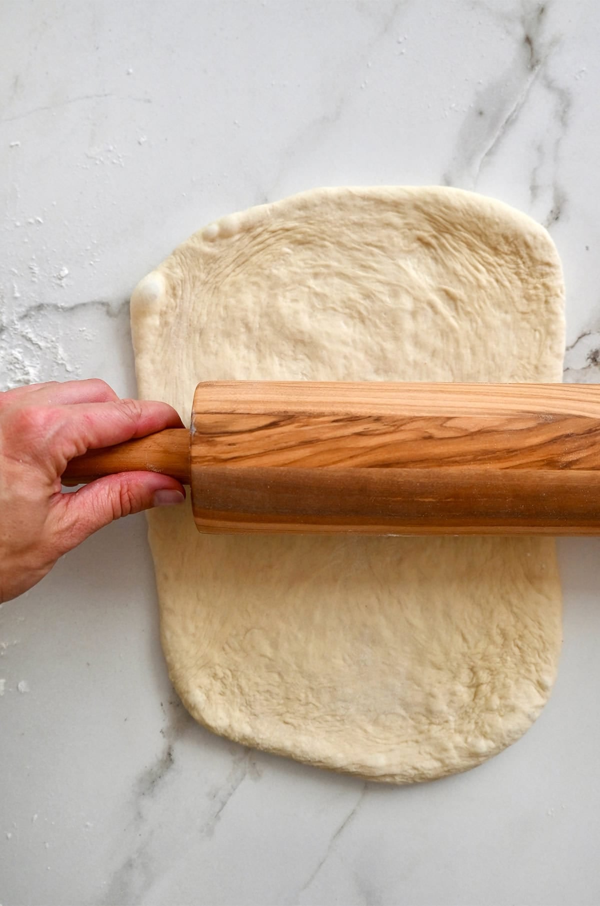 Rolling pizza dough into a 10-inch square.