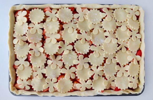 Strawberry slab pie on baking sheet with cutout pie dough shapes prior to baking.