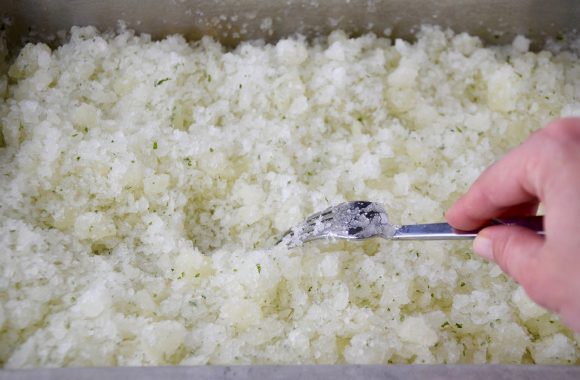 A metal baking pan containing lemon granita being stirred with a metal fork