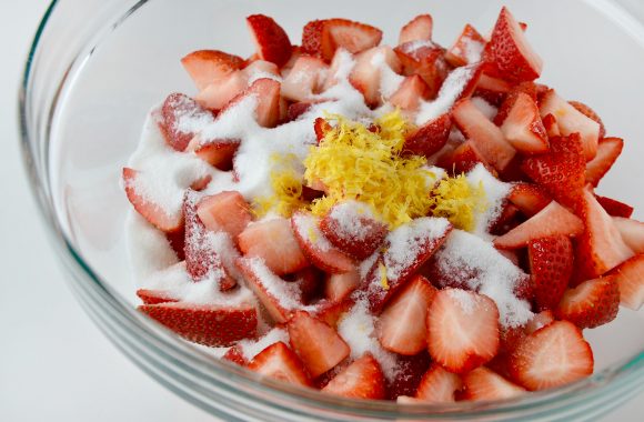 Clear bowl with strawberries, lemon zest and sugar.