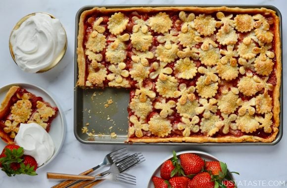 Simple Strawberry Slab Pie with a single serving on a white plate, whipped cream in small bowl, two forks and a bowl of fresh strawberries surrounding it.