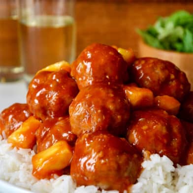 Sweet and sour meatballs with pineapple over steamed white rice in a white dinner bowl.