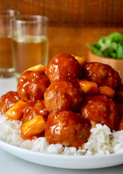 Sweet and sour meatballs with pineapple over steamed white rice in a white dinner bowl.