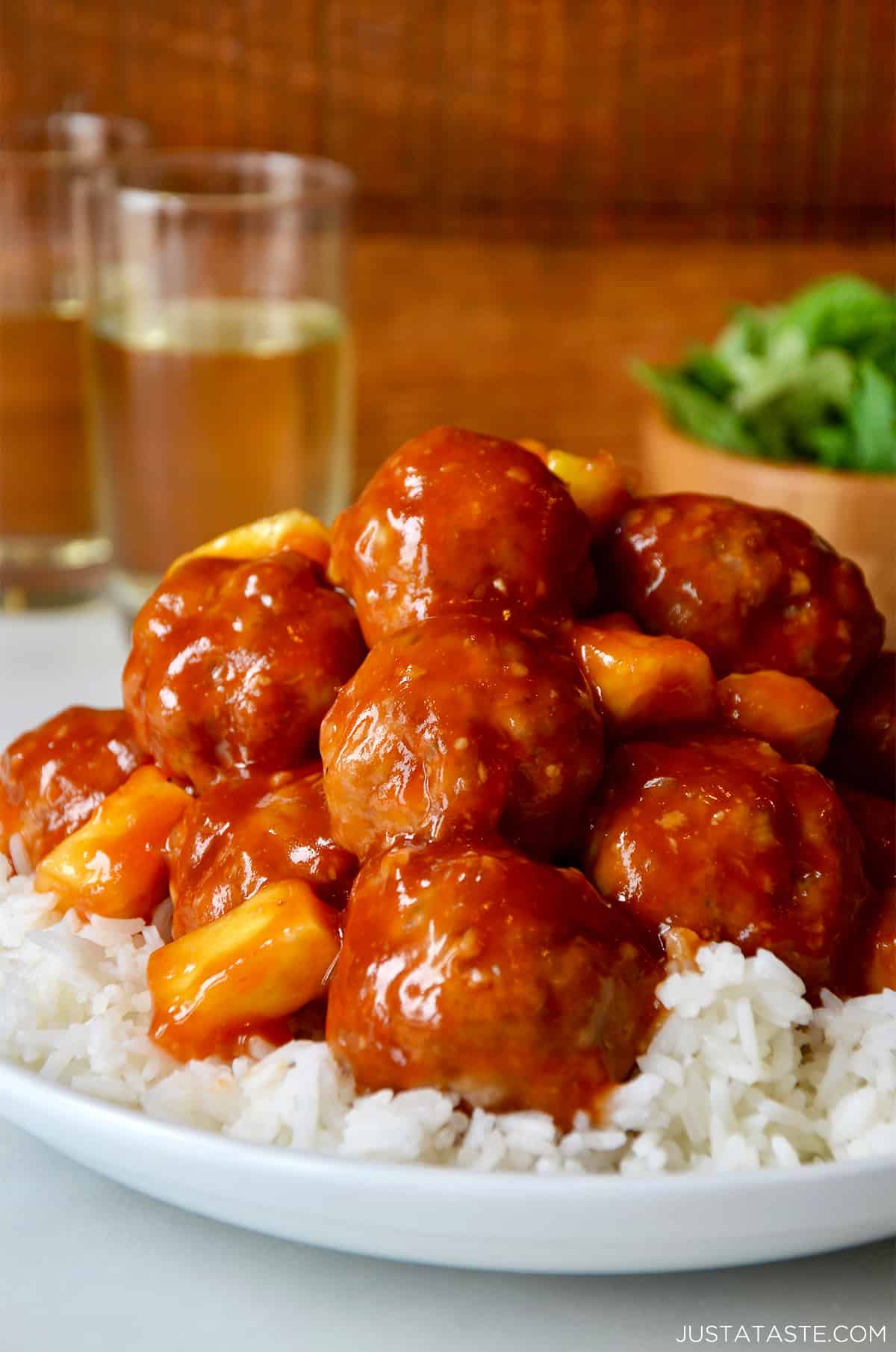 Sweet and sour meatballs with pineapple over steamed white rice in a white dinner bowl.