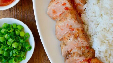 Scallions and Thai sweet chili sauce in small white bowls next to two forks and white serving tray with Sweet and Sour Roast Pork Tenderloin with white rice.