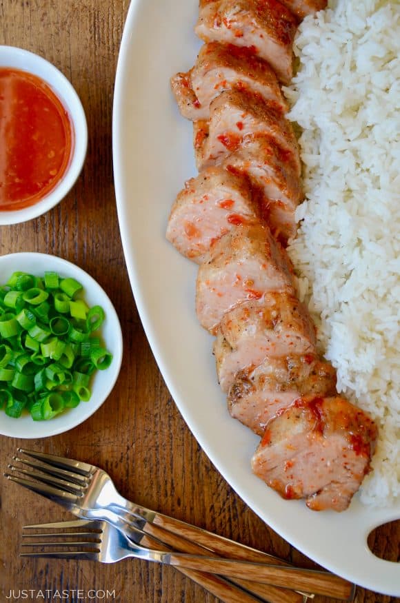 Scallions and Thai sweet chili sauce in small white bowls next to two forks and white serving tray with Sweet and Sour Roast Pork Tenderloin with white rice.