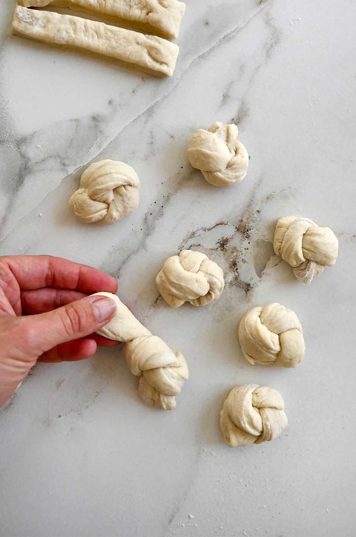 Tying strips of pizza dough into knots.