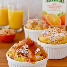 White ramekins filled with brioche bread pudding being drizzled with caramel sauce