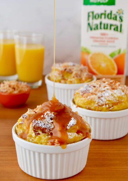 White ramekins filled with brioche bread pudding being drizzled with caramel sauce