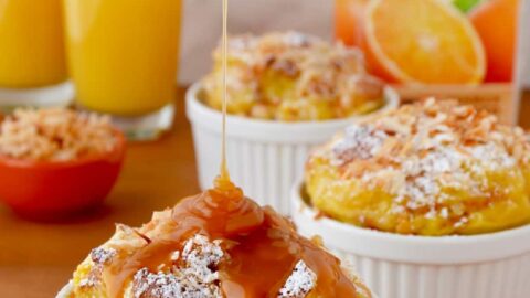 White ramekins filled with brioche bread pudding being drizzled with caramel sauce