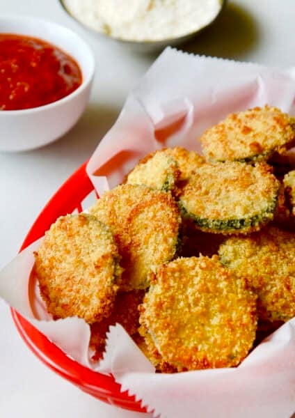 Baked zucchini chips with parmesan in a red food basket lined with parchment paper.