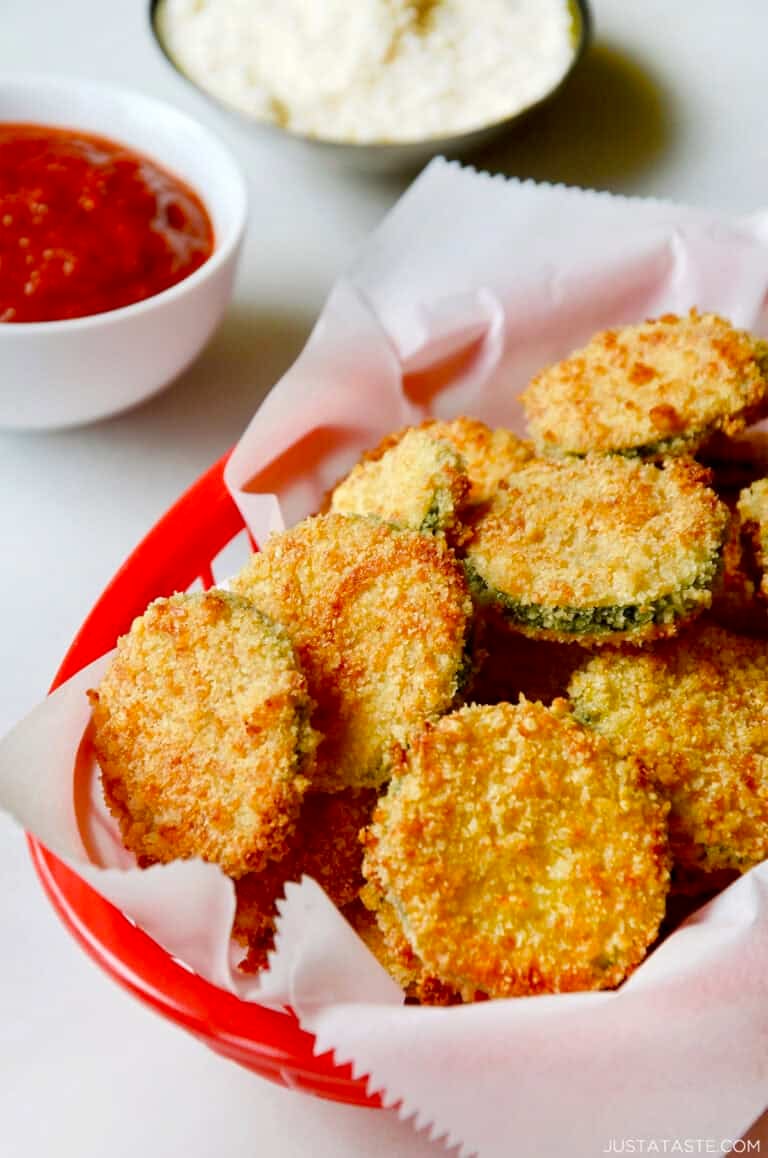 Baked zucchini chips with parmesan in a red food basket lined with parchment paper.