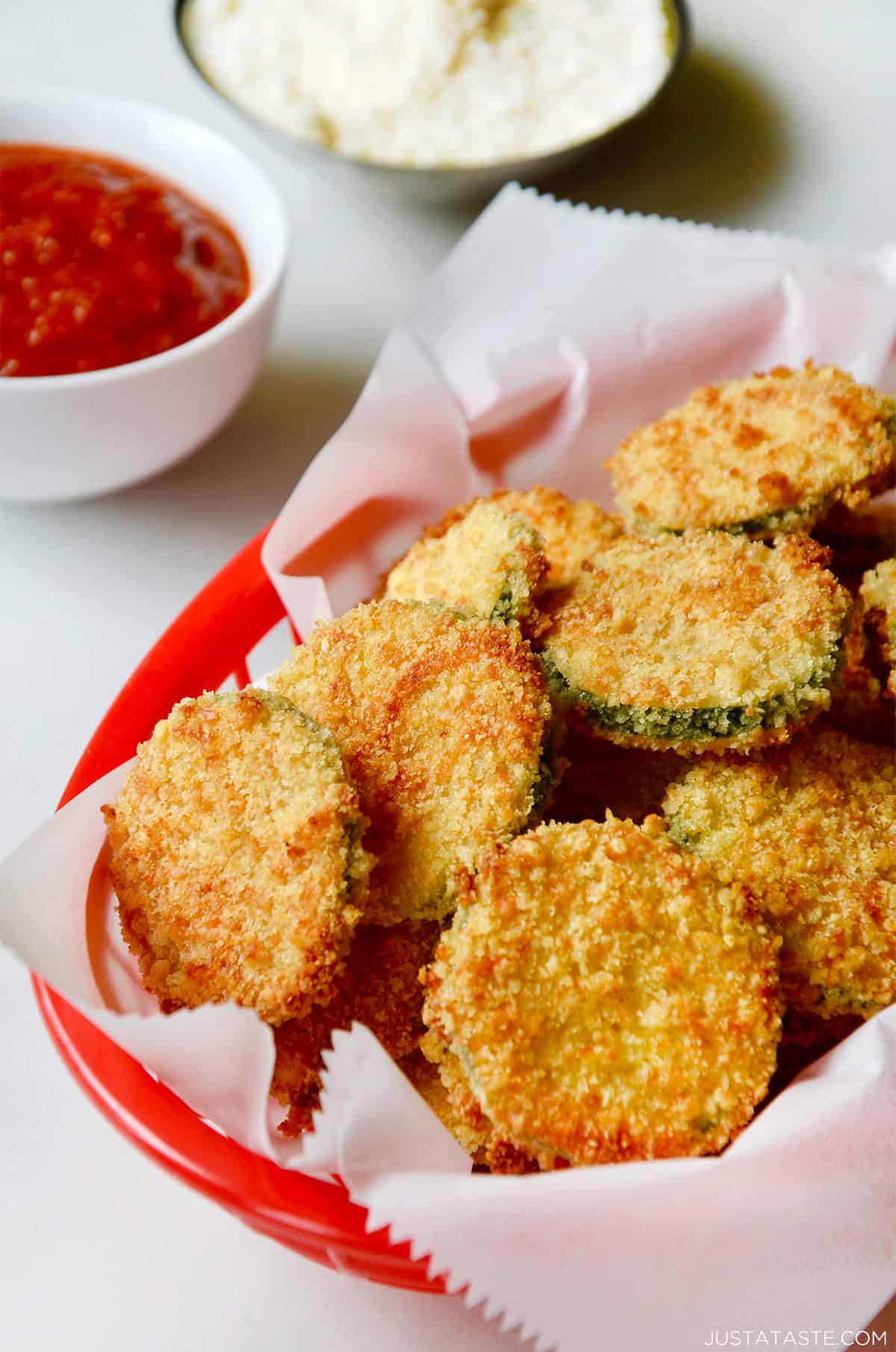 Baked zucchini chips with parmesan in a red food basket lined with parchment paper.