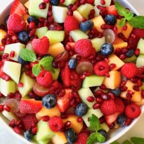 A white bowl containing fruit salad topped with fresh mint leaves