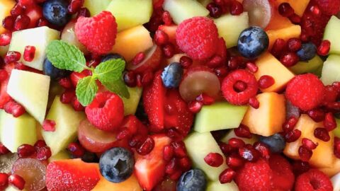 A white bowl containing fruit salad topped with fresh mint leaves