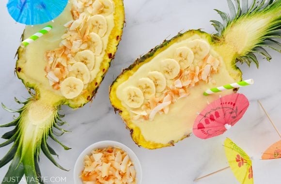 Creamy Coconut Pineapple Smoothies in hollowed out pineapples topped with sliced bananas and coconut