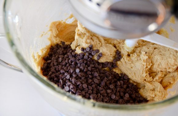 A close-up of a KitchenAid glass stand mixer bowl containing chocolate chip cookie dough 