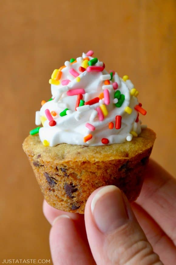 A close-up shot of a hand holding a Chocolate Chip Cookie Cup topped with vanilla frosting and sprinkles