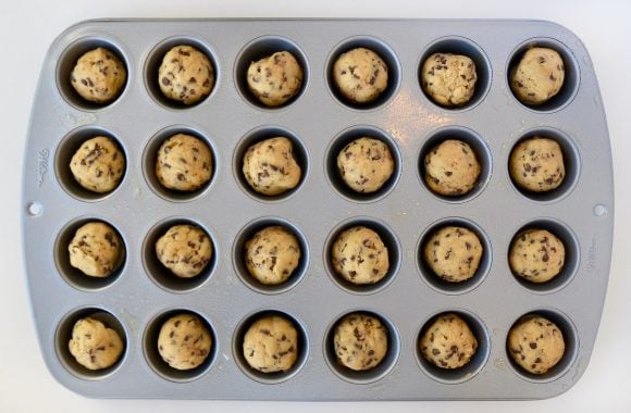 A mini muffin tin containing balls of unbaked chocolate chip cookie dough