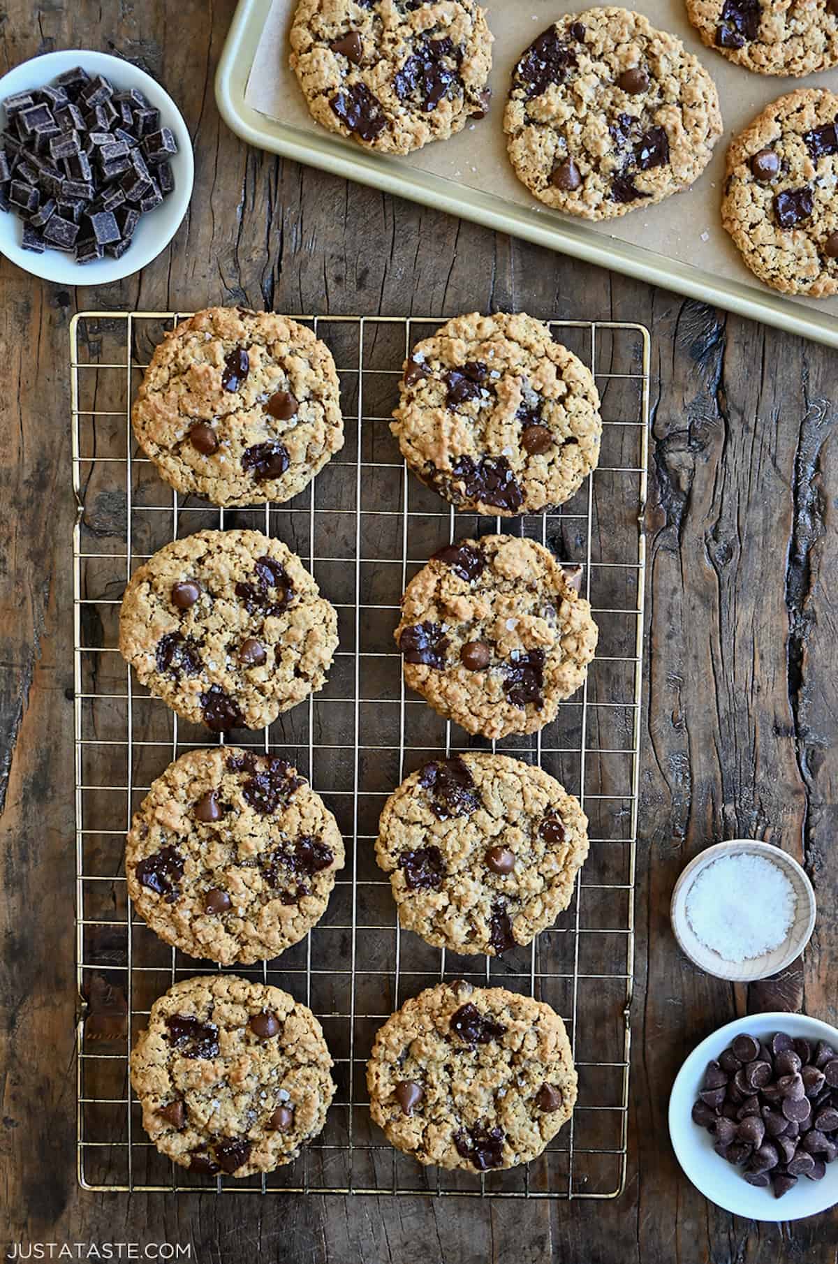 Flourless oatmeal cookies studded with chocolate chips and chunks on a wire cooling rack next to a small bowl containing large-flake sea salt.