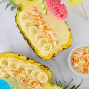 Pineapples hollowed out and filled with smoothie mixture topped with sliced bananas and coconut