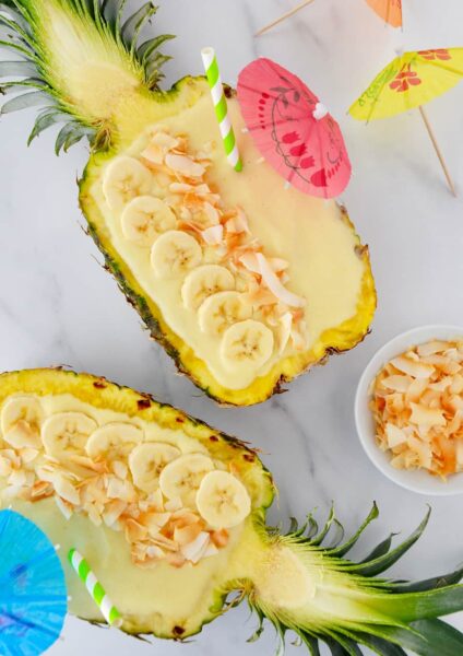 Pineapples hollowed out and filled with smoothie mixture topped with sliced bananas and coconut
