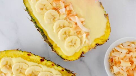 Pineapples hollowed out and filled with smoothie mixture topped with sliced bananas and coconut