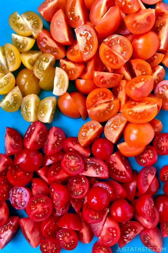 Halved yellow, orange and red cocktail tomatoes on a bright blue background