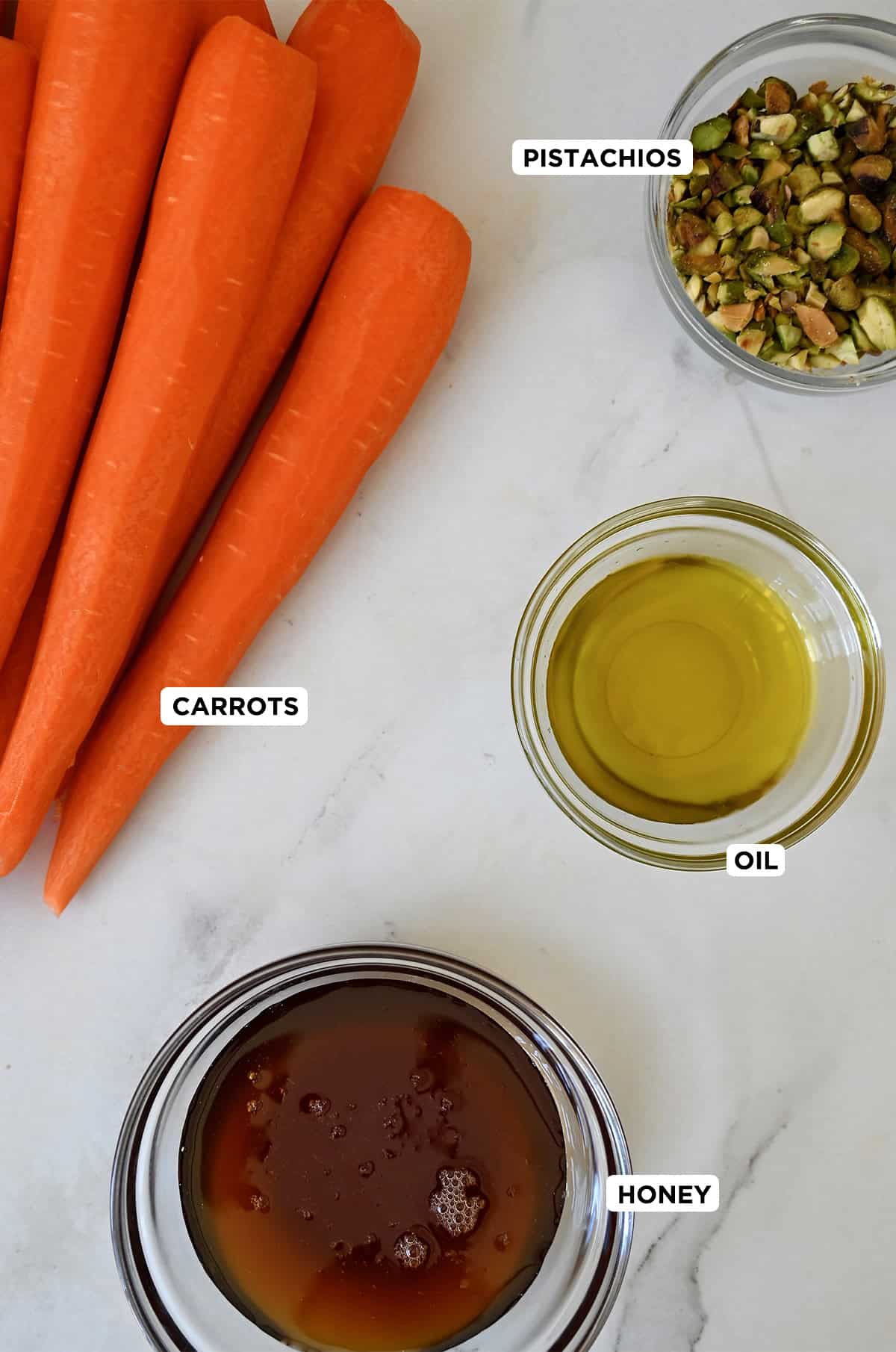Whole, peeled carrots next to a small bowl containing olive oil and another small bowl containing honey.