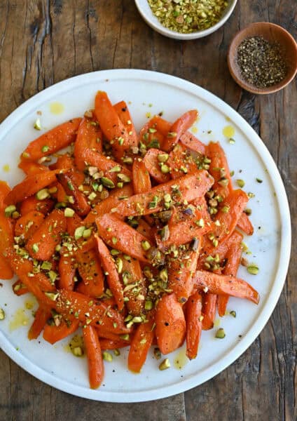Honey roasted carrots garnished with chopped pistachios on a white serving platter.