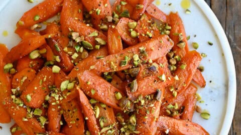 Honey roasted carrots garnished with chopped pistachios on a white serving platter.