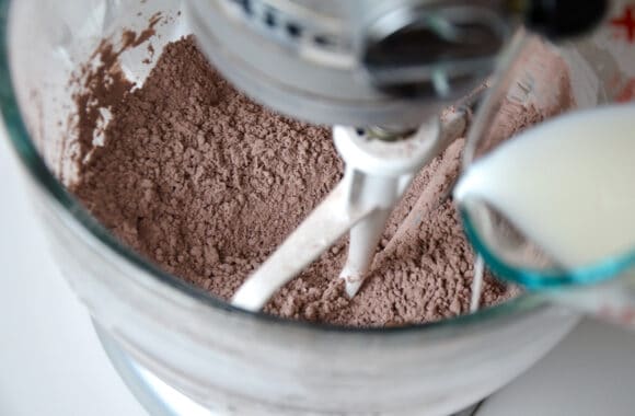 cooca powder in a stand mixer with milk being poured in