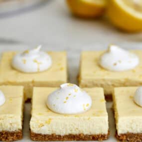 Easy cheesecake bars topped with whipped cream and lemon zest on a white platter.