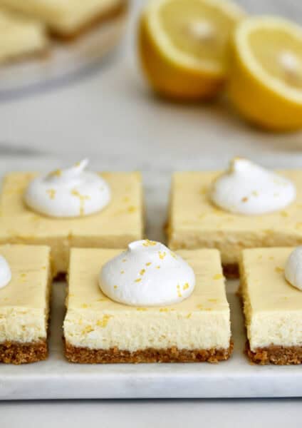 Easy cheesecake bars topped with whipped cream and lemon zest on a white platter.