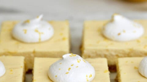 Easy cheesecake bars topped with whipped cream and lemon zest on a white platter.