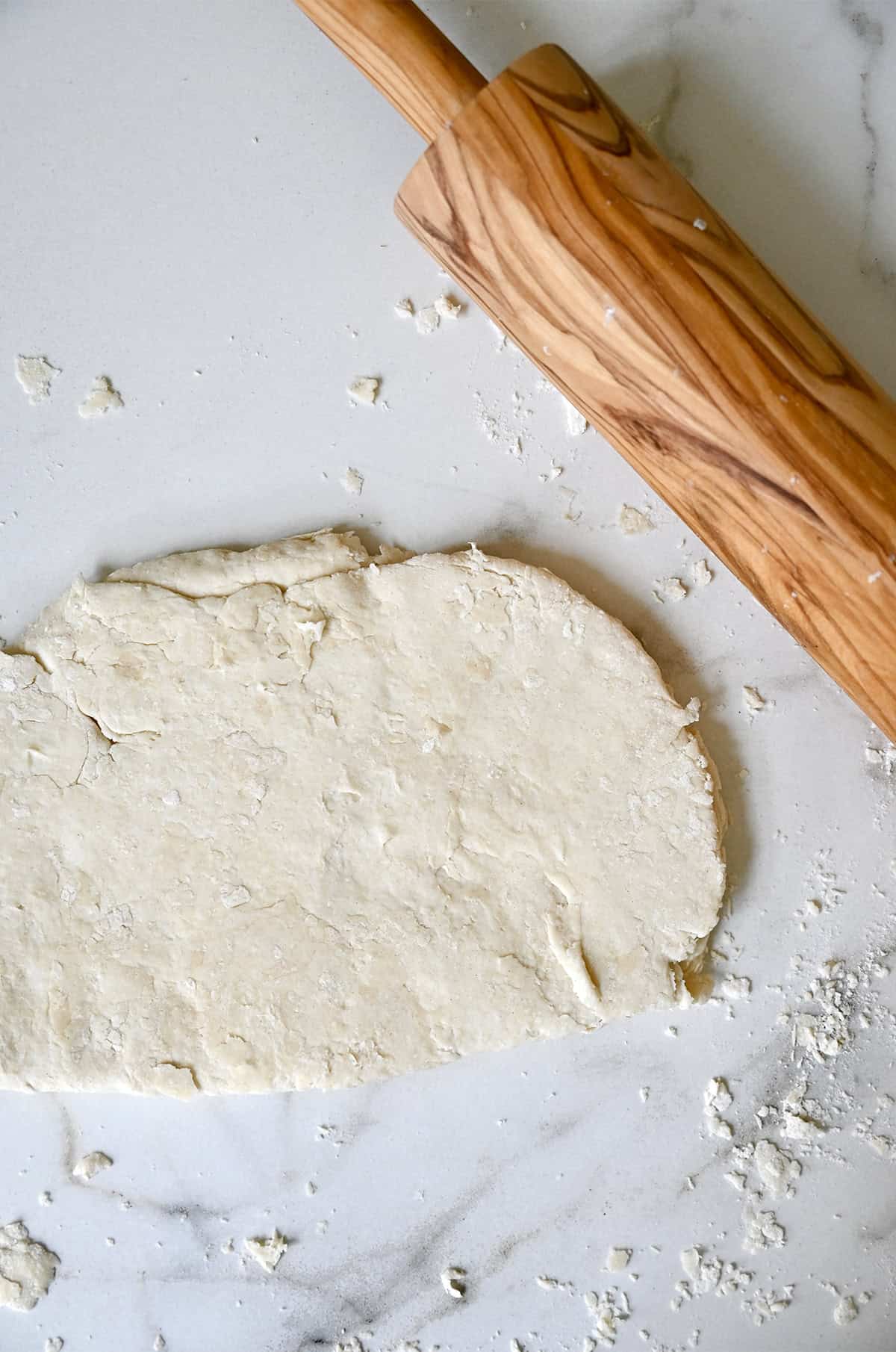Shortcake dough rolled out on a lightly floured surface next to a rolling pin.