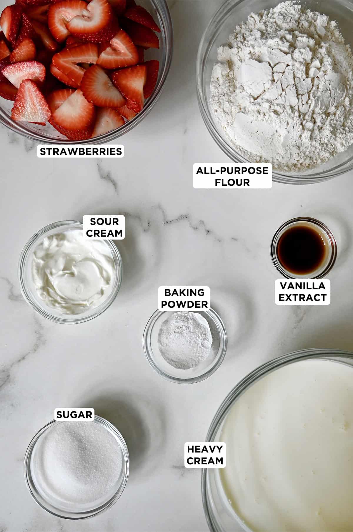 Various sizes of glass bowls containing ingredients to make strawberry shortcake.
