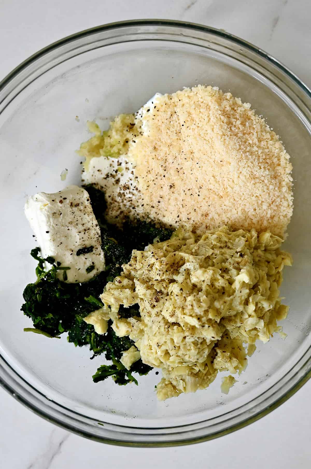 A bowl containing spinach artichoke dip ingredients.