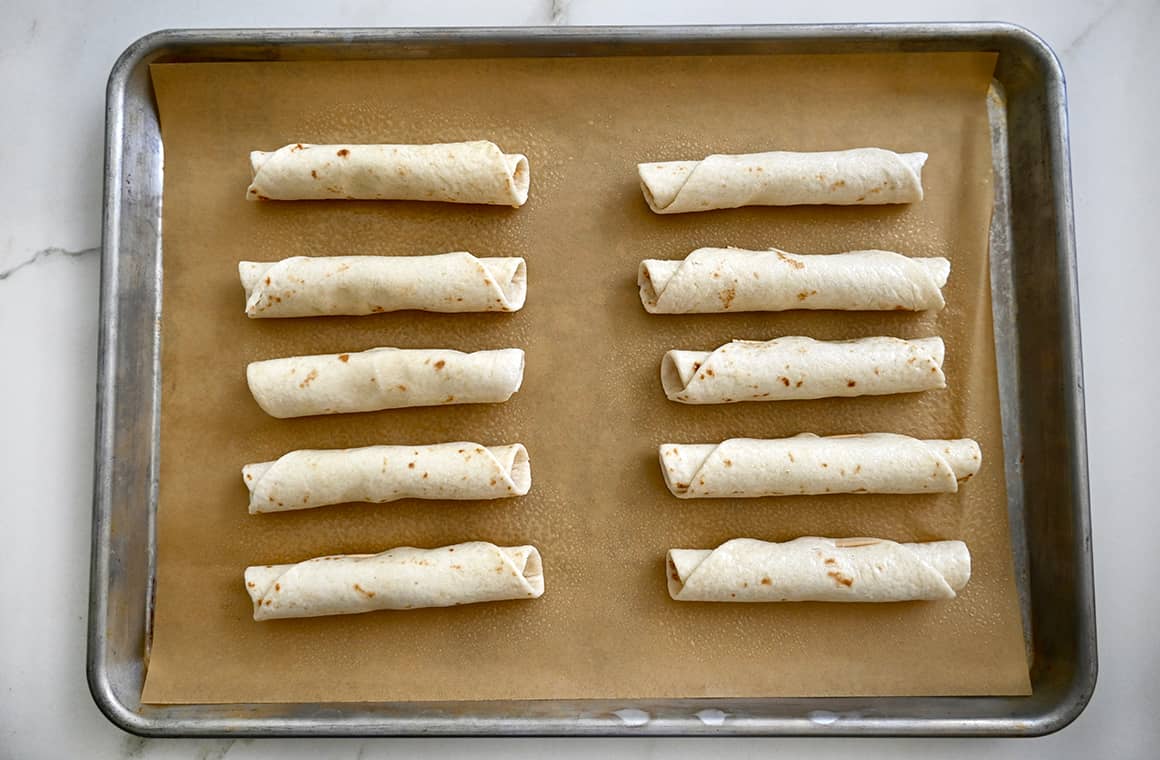 Rolled-up tortillas on a parchment paper-lined baking sheet