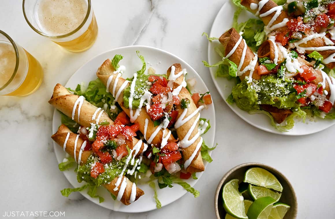 Baked Cheese Taquitos topped with salsa and guacamole and drizzled with queso blanco next to two glasses filled with light beer