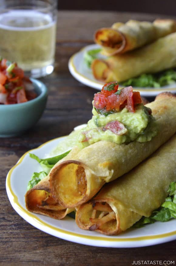 A plate with baked chicken taquitos topped with guacamole and pico de gallo