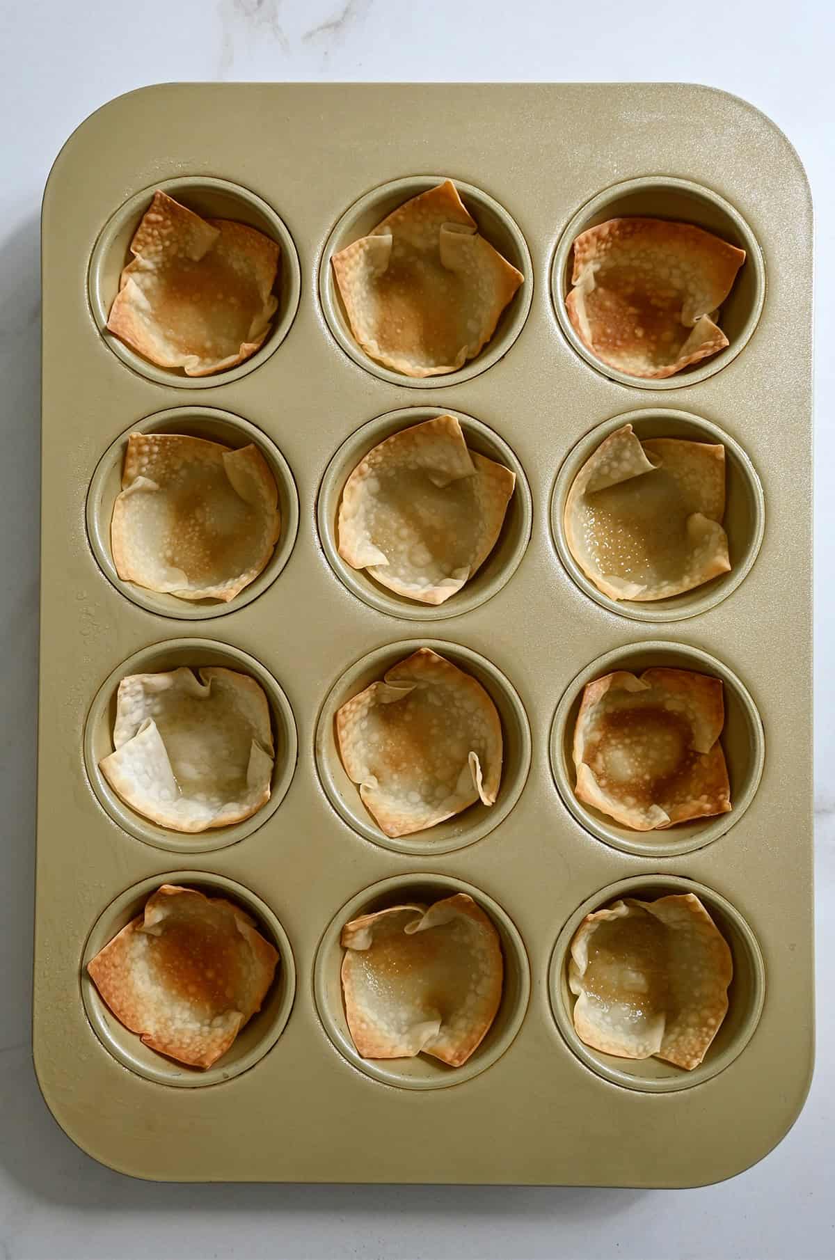 Golden brown baked wonton cups in a muffin pan.