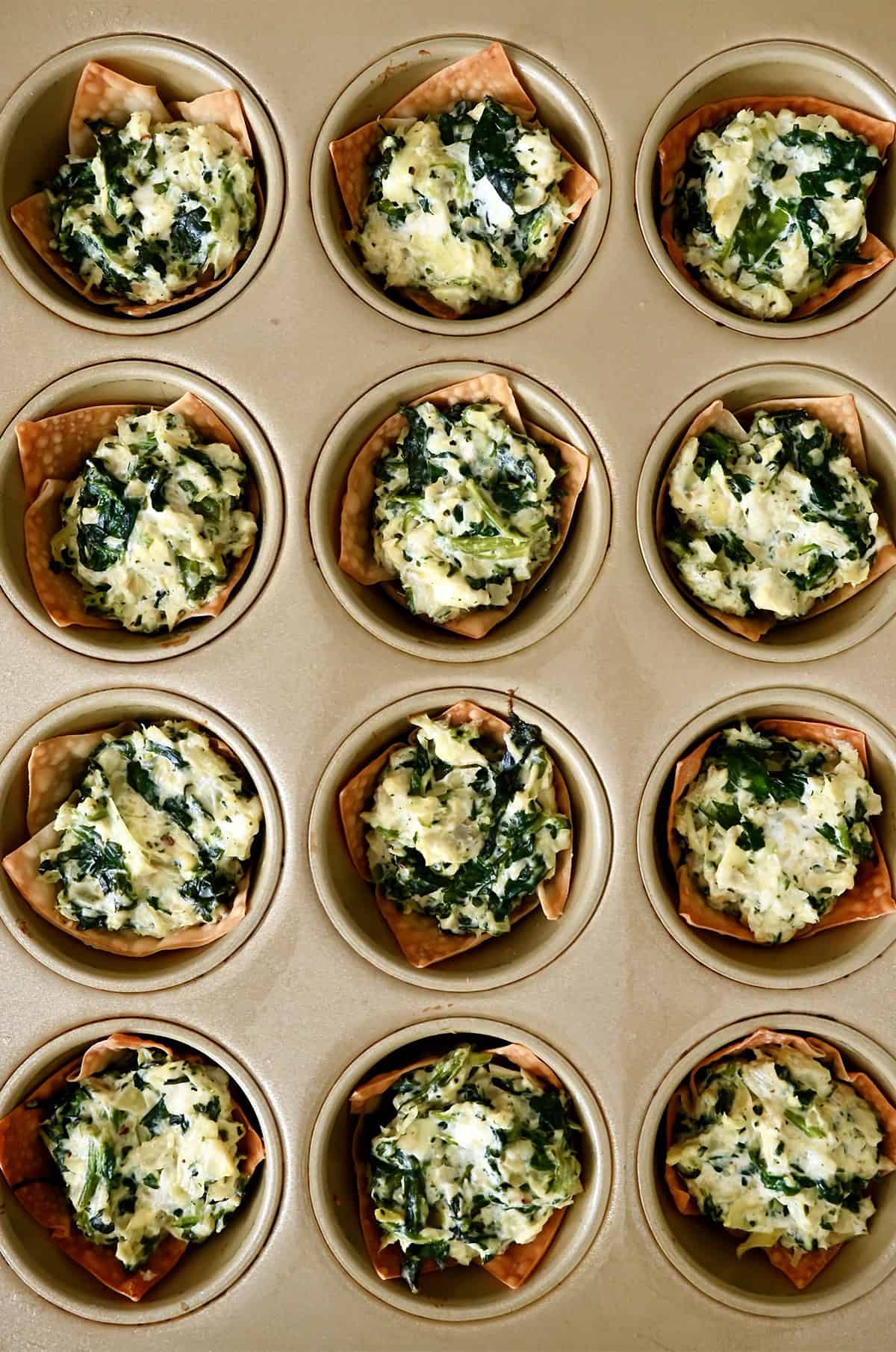 Baked wonton cups filled with spinach artichoke dip filling.