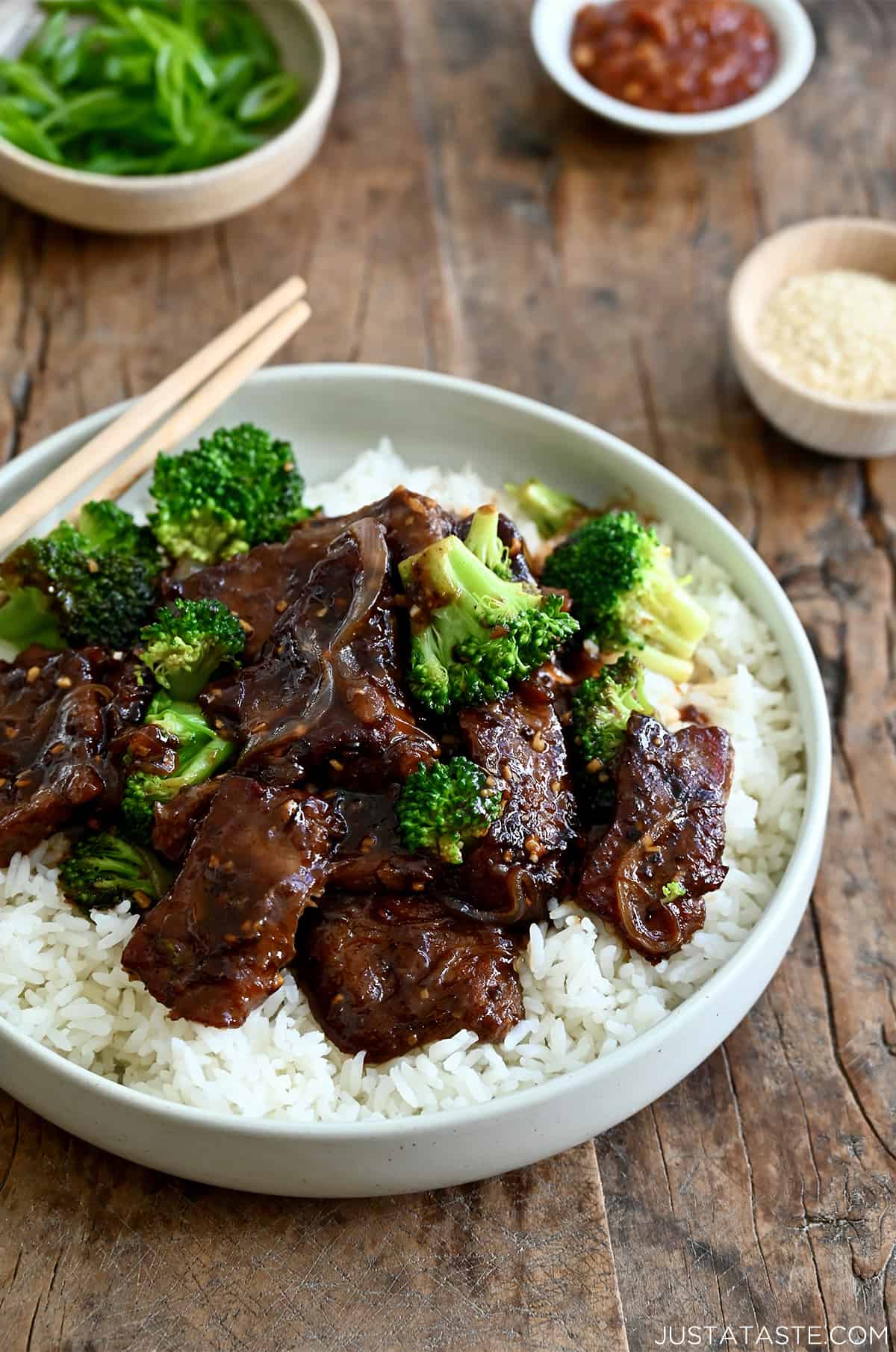 Stir-fried beef and broccoli over a bed of rice on a white plate with chopsticks.